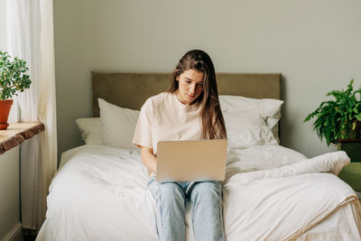 Student sitting on bed typing project in laptop, online learning, remote work from home