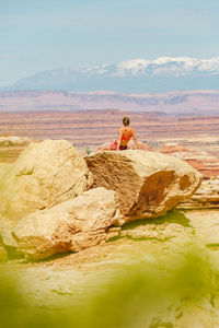Female hiker in sports bra rests on large rock overlooking canyonlands