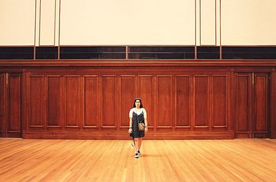 Full length of young woman standing on hardwood floor against wooden wall in room