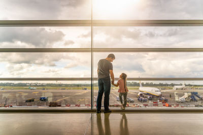 People at airport against sky seen through glass window