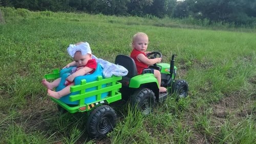 Baby sister sitting in the back of the tractor while big brother drives through the field