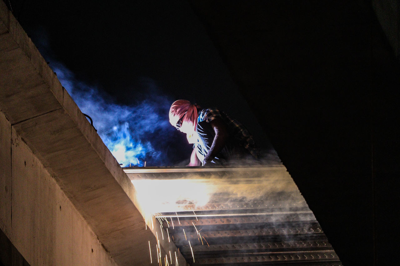 LOW ANGLE VIEW OF PERSON STANDING AGAINST WALL AT NIGHT