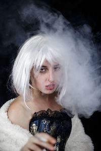 Portrait of female model smoking cigarette against black background