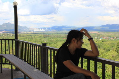 Woman sitting on railing by balcony against sky