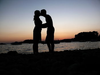 Silhouette couple standing by sea against clear sky during sunset