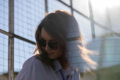 Close-up of young woman against glass window during sunny day