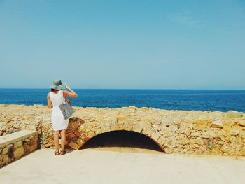 Rear view of woman standing on beach against clear sky