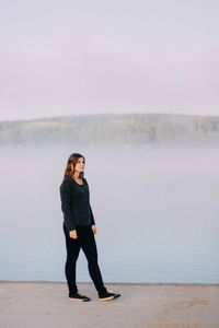 Full length of young woman standing against lake during foggy weather