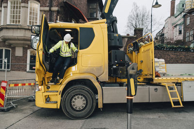 Full length of female building contractor coming out of construction vehicle