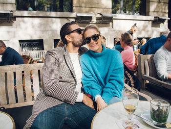 Man kissing woman while sitting at outdoor restaurant