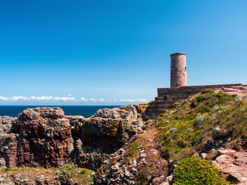 Old building by sea against clear blue sky