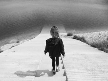 Rear view of woman moving down on steps towards lake