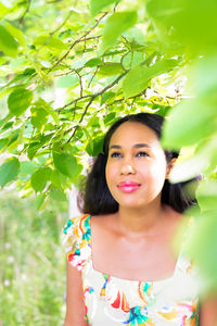 Portrait of a mixed race african american woman standing under a tree with bright green leaves