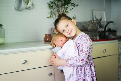 Cute european kid girl with baby doll in sling. motherhood and role-playing, child development