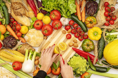 A young girl who is cutting a lemon on a kitchen table with various vegetables