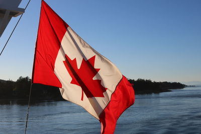 Canadian flag by lake against clear blue sky