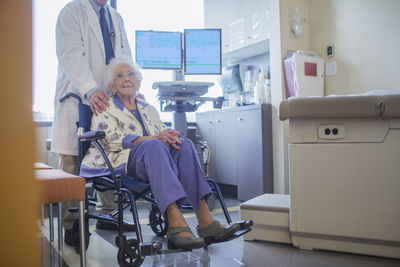 Low section of doctor standing by patient sitting on wheelchair in hospital