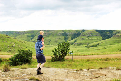 Father carrying son on shoulders standing against sky