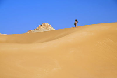Low angle view of man climbing sandy hill at desert against clear sky