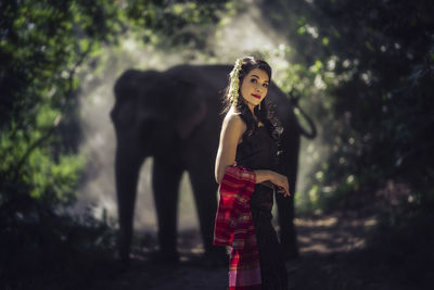 Portrait of woman standing by tree in forest