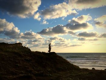 Man and woman with dog standing by sea against cloudy sky