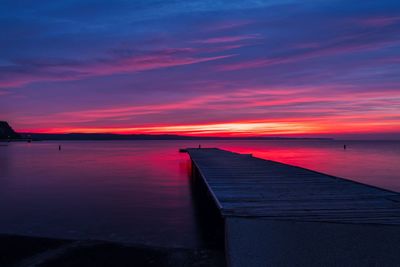 Pier over sea against orange sky