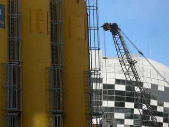 Low angle view of crane and industrial building against sky