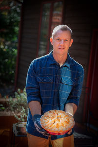 Portrait of mature man holding sweet pie outside house