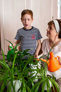 Grandmother and her little grandson red-haired boy 6-7 years old watering flowers together.