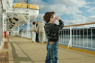 Boy looking through binocular while standing on yacht