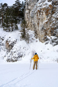 Rear view of young woman in yellow clothes with backpack skiing against mountain winter sport 