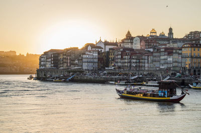 Boats in river against buildings in city at sunset