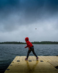 A boy throws a rock into the lake from a dock on a cloudy day