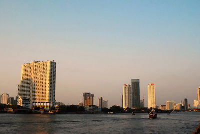 Modern buildings by river against clear sky