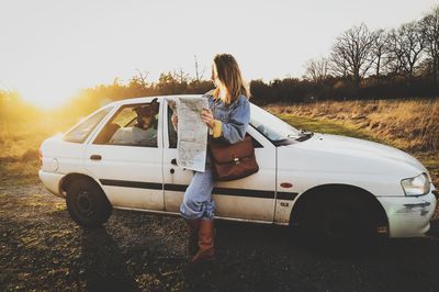 Woman standing by car on field against sky