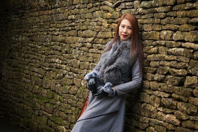 Portrait of smiling woman leaning on stone wall during winter