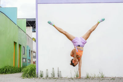 Woman talking on mobile phone while doing handstand in front of wall
