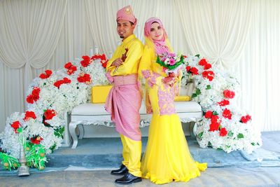 Portrait of bride and bridegroom standing against flower decorations during ceremony