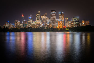 Illuminated buildings by river against sky at night