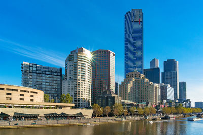 Modern buildings by river against blue sky