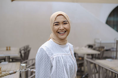 Cheerful young woman standing outside cafe