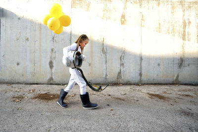 Full length of a boy holding balloon standing against wall