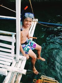 High angle portrait of smiling man wearing snorkel sitting on jetty over river