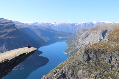 Rear view of man sitting on cliff against mountains