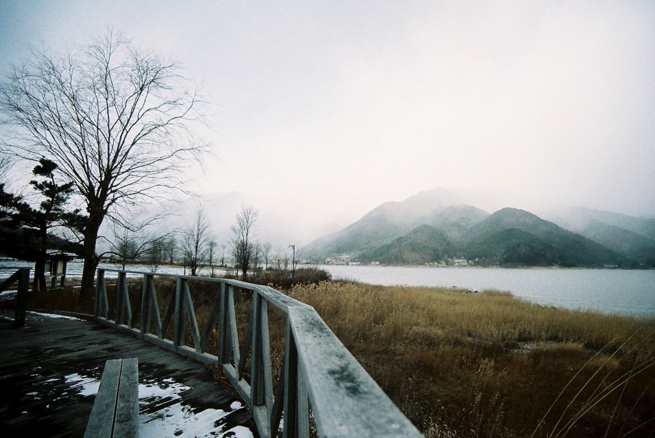 water, mountain, clear sky, tranquility, tranquil scene, scenics, nature, lake, mountain range, beauty in nature, copy space, sky, landscape, transportation, river, day, non-urban scene, railing, grass, outdoors