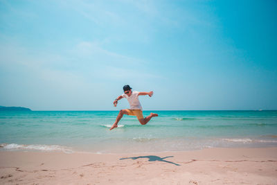 Full length of young man jumping at beach against blue sky