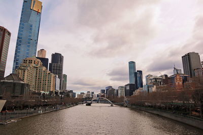 Modern buildings by river against sky in city