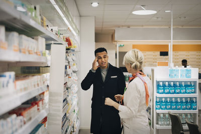 Male customer explaining headache to female pharmacist standing by rack at store