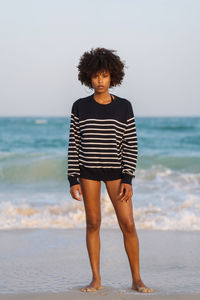 Young black woman standing by the sea wearing striped jumper