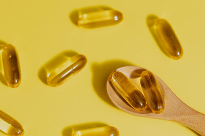 Omega-3 fish oil capsules in the wooden spoon on yellow background for healthcare concept
